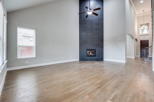 unfurnished living room with light wood finished floors, baseboards, a tile fireplace, high vaulted ceiling, and ceiling fan with notable chandelier