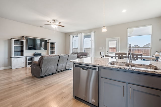 kitchen featuring stainless steel dishwasher, a sink, a wealth of natural light, and light stone countertops