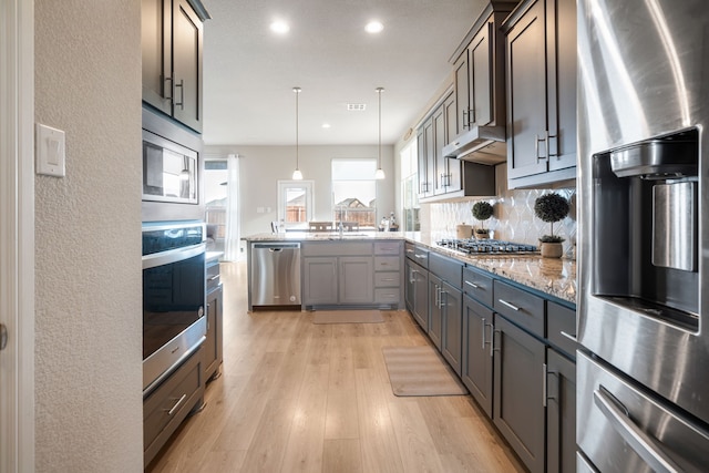 kitchen featuring light stone counters, under cabinet range hood, stainless steel appliances, a peninsula, and light wood-style floors