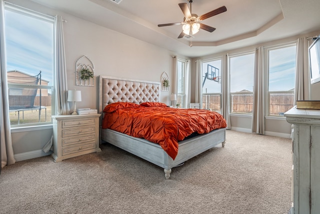 bedroom with a tray ceiling, light colored carpet, baseboards, and multiple windows