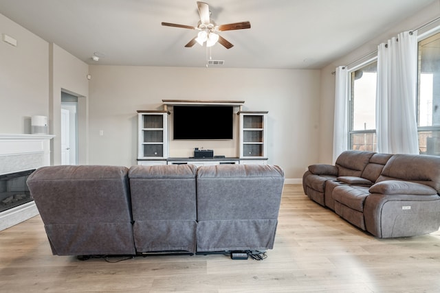 living room with baseboards, visible vents, a ceiling fan, a glass covered fireplace, and light wood-style flooring