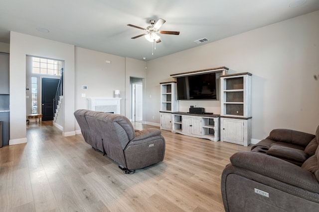 living room featuring a fireplace, visible vents, a ceiling fan, light wood-type flooring, and baseboards