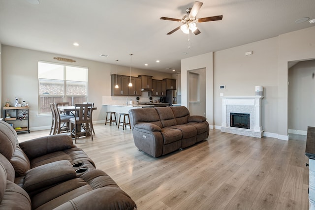 living room featuring a ceiling fan, a stone fireplace, light wood-style flooring, and baseboards