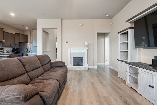 living room featuring recessed lighting, visible vents, light wood-style flooring, a glass covered fireplace, and baseboards