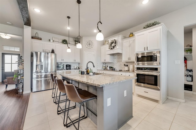 1016 Northern Oaks Ct, Springtown, TX 76082 - kitchen featuring stainless steel appliances, tasteful backsplash, light stone counters, a kitchen island with sink, and a kitchen bar
