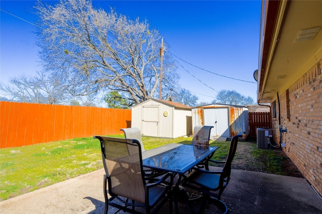 view of patio / terrace featuring central air condition unit, a storage unit, outdoor dining space, a fenced backyard, and an outdoor structure