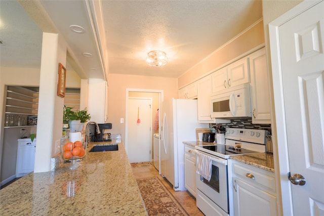 kitchen featuring a textured ceiling, light stone counters, white appliances, a sink, and white cabinets