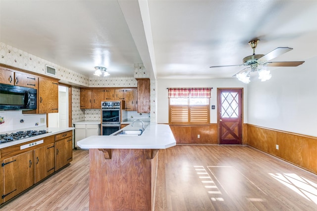 kitchen featuring brown cabinetry, a wainscoted wall, a sink, and black appliances