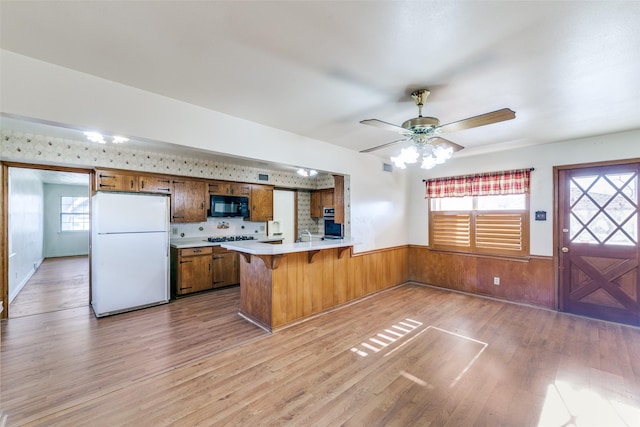 kitchen featuring black microwave, a wainscoted wall, a peninsula, freestanding refrigerator, and brown cabinets