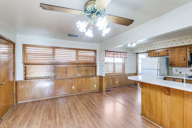 kitchen with brown cabinets, visible vents, light wood-style flooring, freestanding refrigerator, and wainscoting