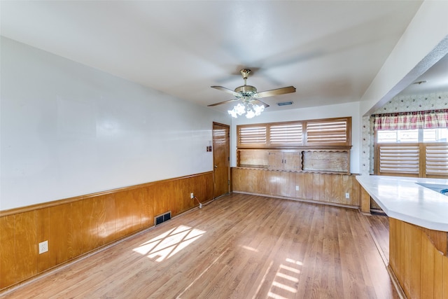 interior space with ceiling fan, a wainscoted wall, wood walls, visible vents, and light wood-type flooring