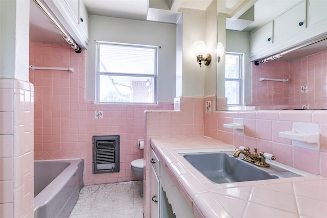 full bathroom with toilet, vanity, tile walls, heating unit, and a tub