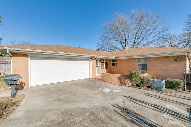 ranch-style home with central air condition unit, a garage, brick siding, concrete driveway, and roof with shingles