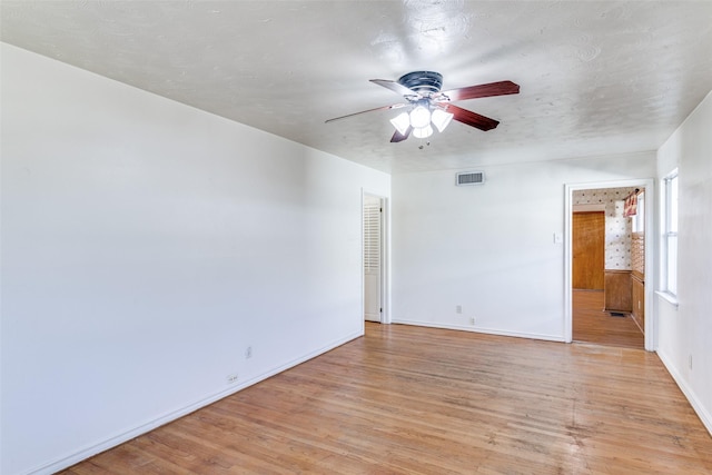 empty room with light wood-style floors, visible vents, ceiling fan, and baseboards