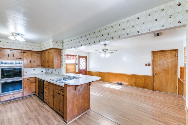 kitchen featuring brown cabinets, visible vents, wainscoting, a sink, and a peninsula