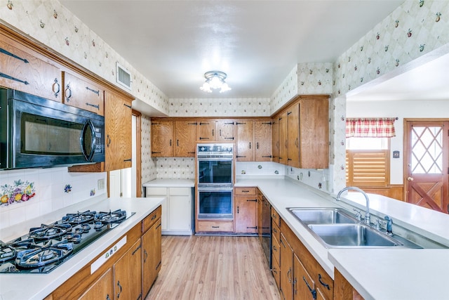 kitchen with brown cabinets, visible vents, a sink, black appliances, and wallpapered walls