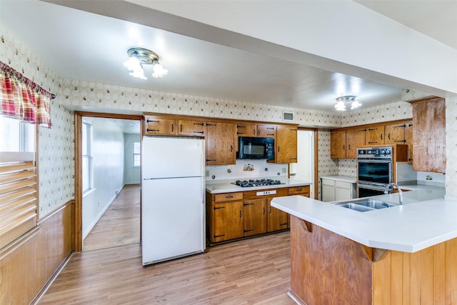 kitchen featuring a sink, black appliances, brown cabinetry, and wallpapered walls