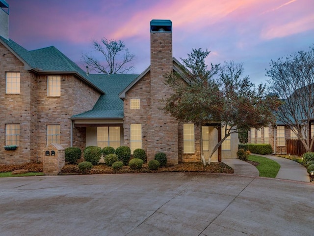 view of front of property featuring brick siding, a chimney, and roof with shingles