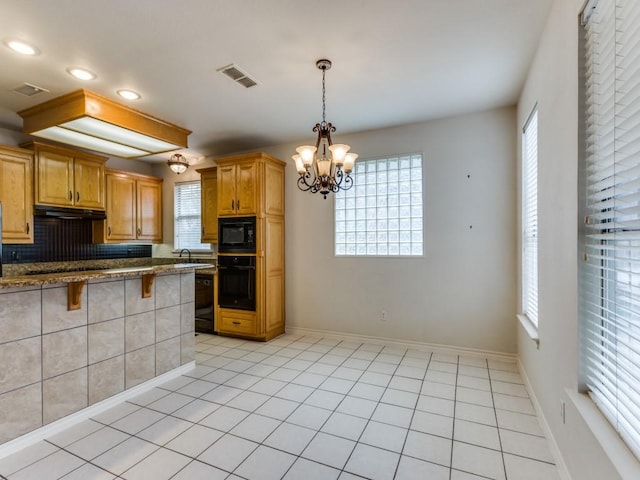 kitchen with light tile patterned floors, a breakfast bar area, an inviting chandelier, under cabinet range hood, and black appliances