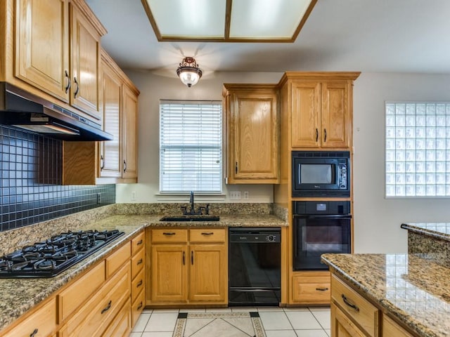 kitchen featuring a sink, light stone countertops, under cabinet range hood, black appliances, and backsplash