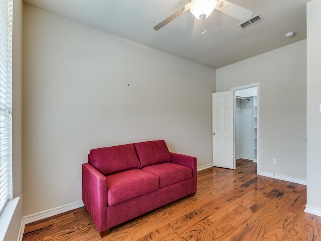 sitting room with a ceiling fan, visible vents, baseboards, and wood finished floors