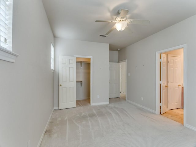 unfurnished bedroom featuring baseboards, a walk in closet, visible vents, and light colored carpet