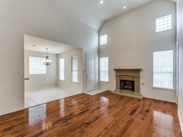 unfurnished living room featuring a chandelier, a fireplace, a towering ceiling, and wood finished floors