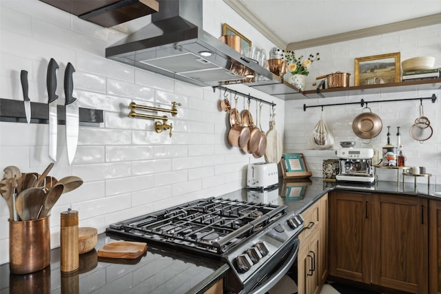 kitchen with wall chimney range hood, open shelves, tasteful backsplash, gas range, and crown molding