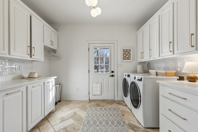 washroom featuring cabinet space, washing machine and dryer, baseboards, and stone tile flooring