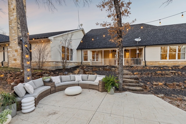 back of property at dusk with stone siding, a shingled roof, a patio, and an outdoor living space