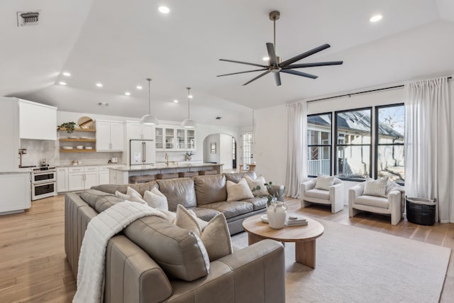 living area featuring light wood-style flooring, vaulted ceiling, visible vents, and arched walkways