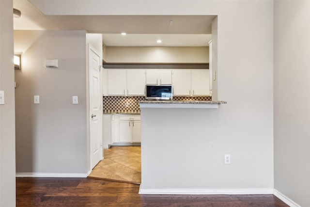 kitchen featuring light wood-style floors, white cabinets, stainless steel microwave, and backsplash