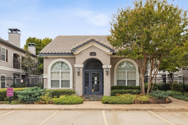 view of front of house with uncovered parking, a tile roof, fence, and stucco siding