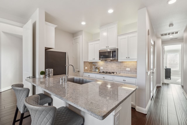 kitchen with visible vents, backsplash, stainless steel appliances, white cabinetry, and a sink