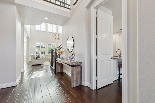 hall featuring a chandelier, baseboards, a high ceiling, and wood finish floors