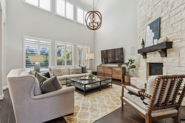 living area featuring a stone fireplace, a high ceiling, an inviting chandelier, and wood finished floors