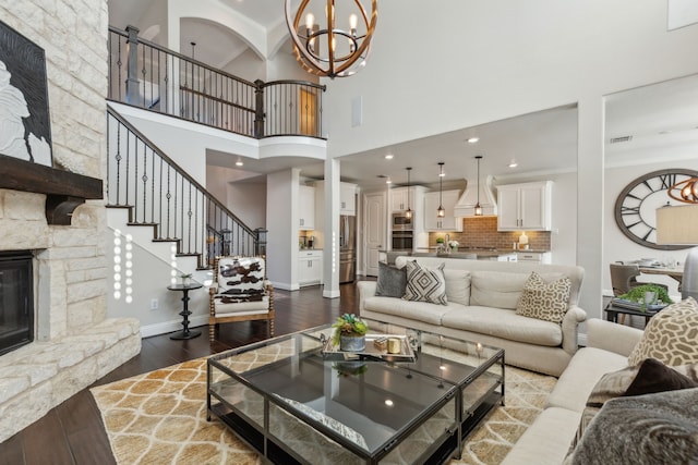 living room with dark wood finished floors, stairway, a stone fireplace, baseboards, and a chandelier