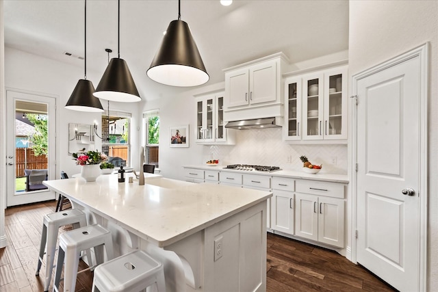 kitchen with white cabinetry, decorative backsplash, stainless steel gas stovetop, dark wood-style floors, and a center island with sink