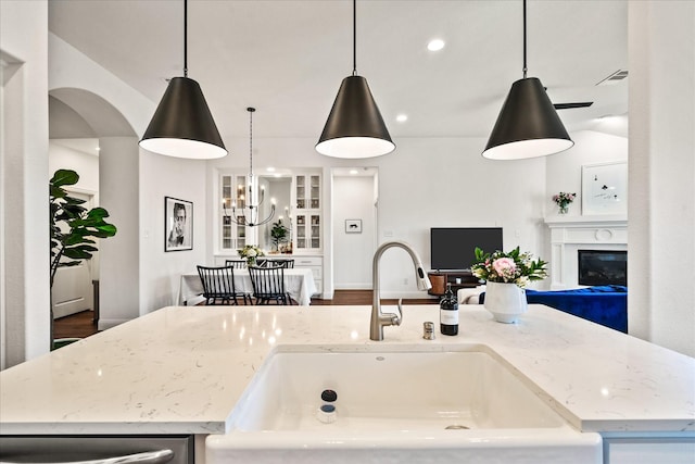 kitchen featuring a glass covered fireplace, light stone counters, open floor plan, and a sink
