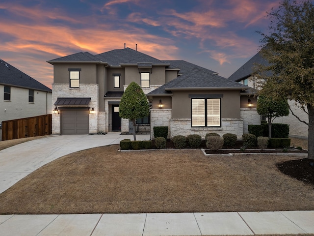 prairie-style home featuring a garage, fence, driveway, stone siding, and stucco siding