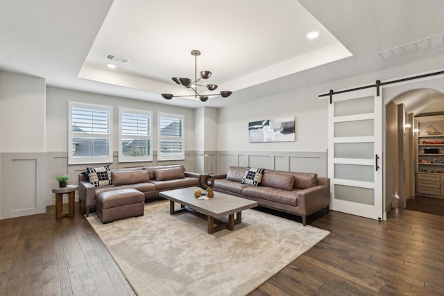 living room featuring built in features, a raised ceiling, dark wood-type flooring, and a barn door