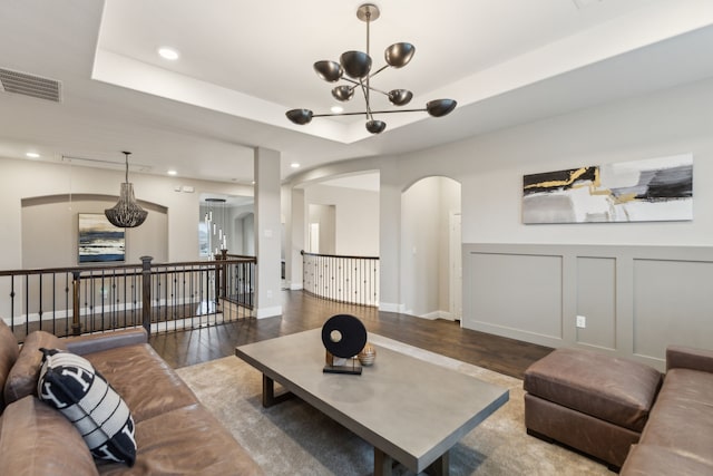 living area featuring visible vents, wood finished floors, an inviting chandelier, a tray ceiling, and a decorative wall