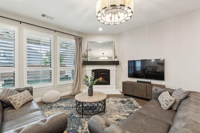 living room with a notable chandelier, wood finished floors, visible vents, baseboards, and a glass covered fireplace