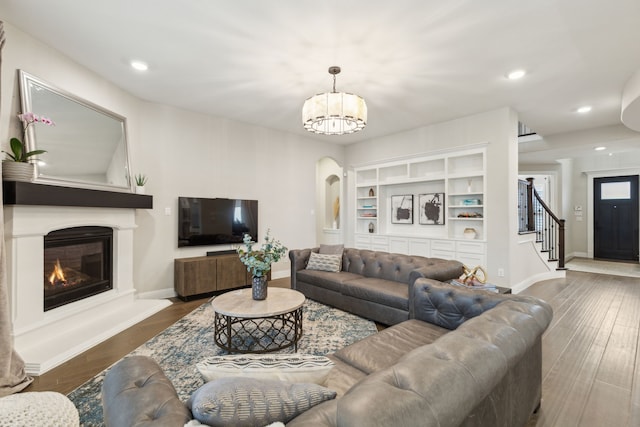 living room with stairway, an inviting chandelier, a glass covered fireplace, wood finished floors, and baseboards