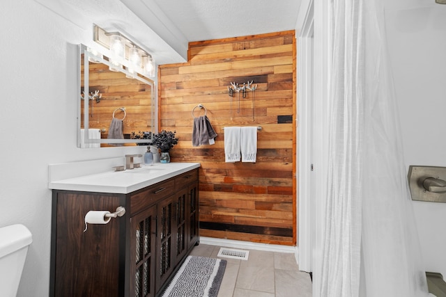 bathroom with visible vents, toilet, tile patterned floors, vanity, and wood walls