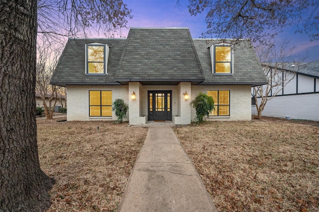 view of front of house with mansard roof, a shingled roof, and brick siding