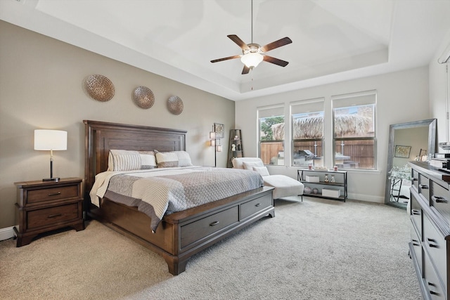 bedroom with a ceiling fan, a raised ceiling, light carpet, and baseboards