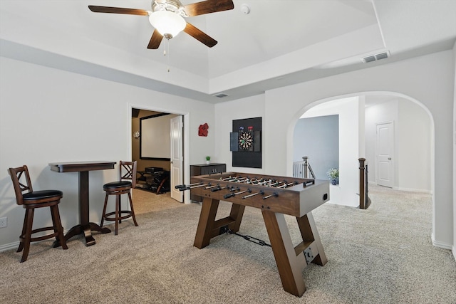 recreation room with arched walkways, light colored carpet, visible vents, baseboards, and a raised ceiling