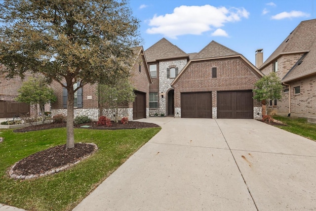 view of front of property featuring a garage, stone siding, driveway, and brick siding