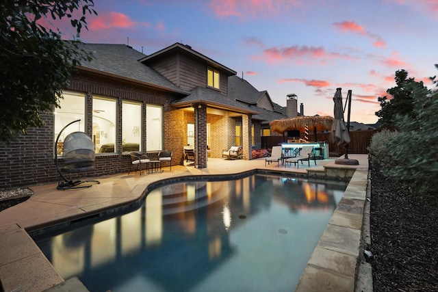 pool at dusk featuring a patio area, fence, and an outdoor pool